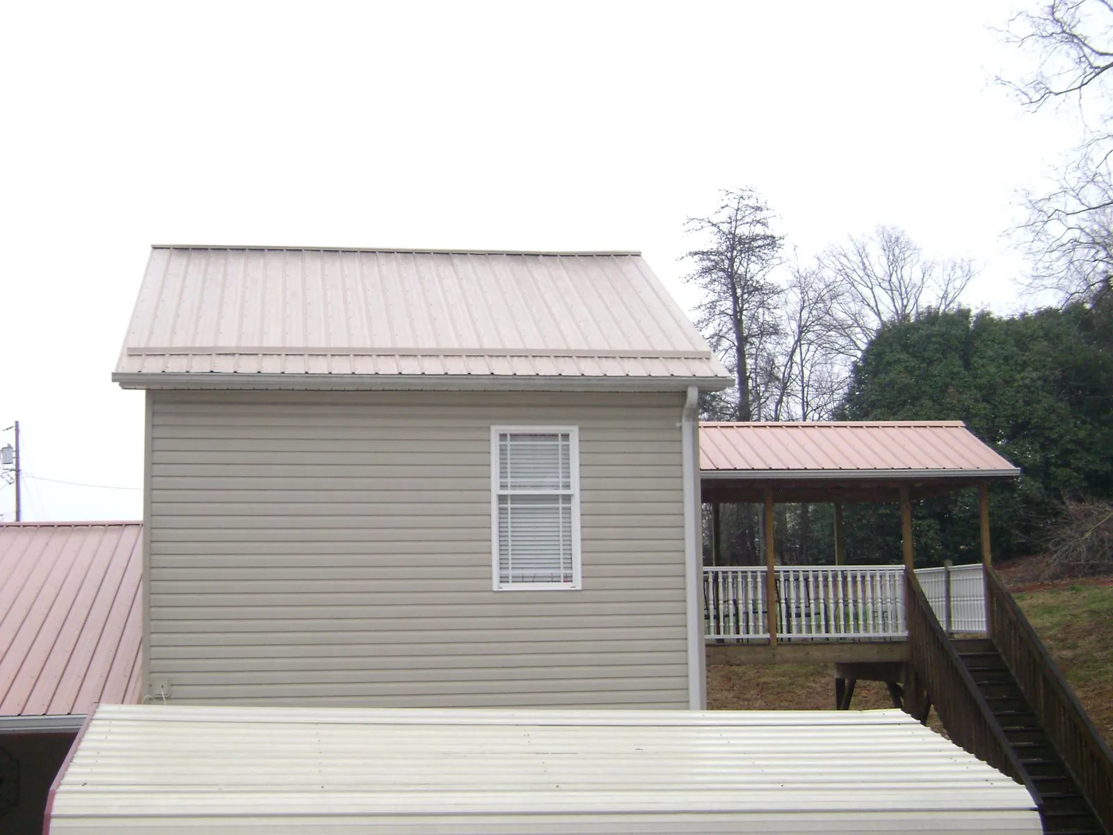 Tan metal roofs on a two story addition and attached porch, from a Roof Replacement job in Clinton
